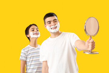 Poster - Man and his little son with shaving foam on faces looking in mirror against yellow background