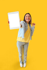 Wall Mural - Happy young woman with big tablet computer on yellow background