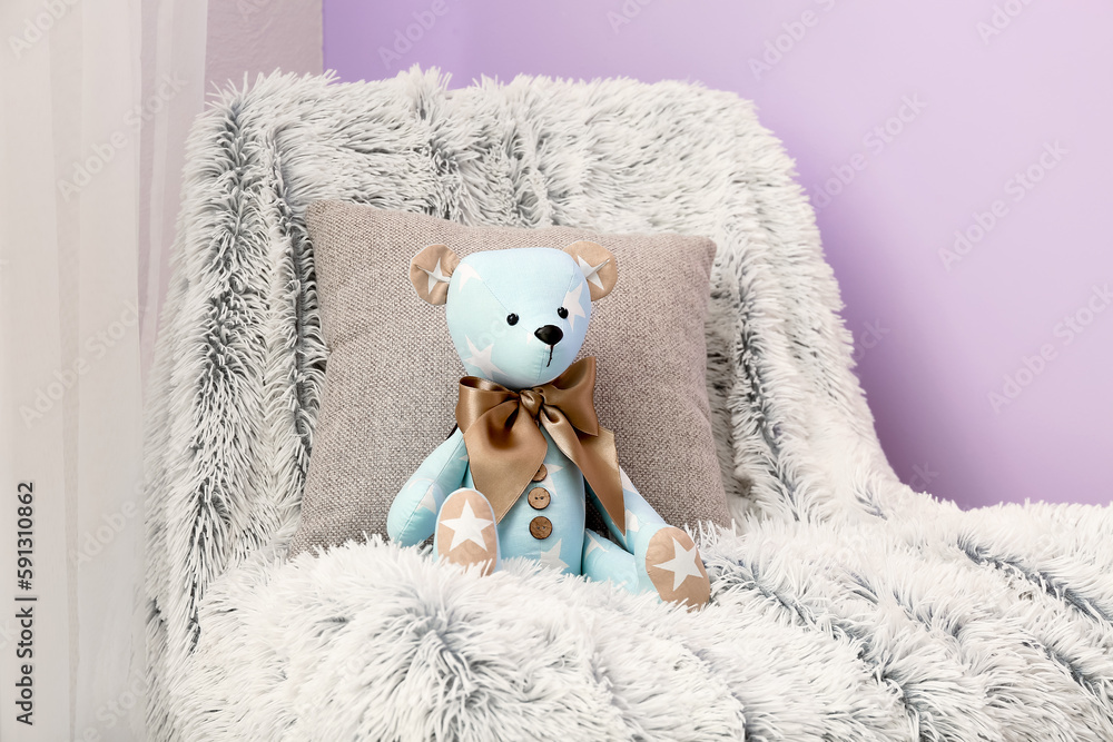 Toy bear with pillow and plaid on chair in room