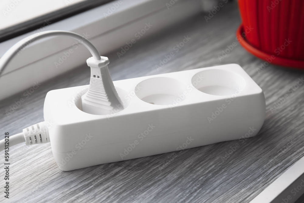 Electric extension cord with plugs on wooden windowsill
