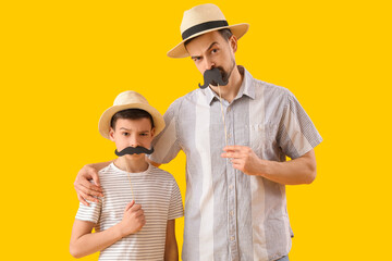 Poster - Portrait of funny father and his little son with paper mustache on yellow background