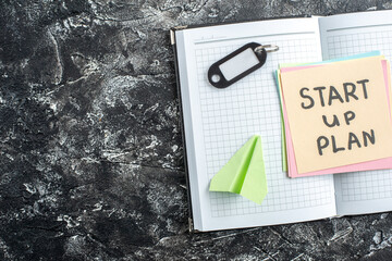 Wall Mural - top view start up plan note on sticker inside open copybook on a gray background lesson student note