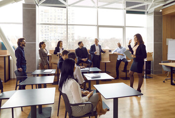 Group of people having business training class. Team of young and mature male and female students sitting or standing in office and listening to experienced teacher sharing knowledge and guidance