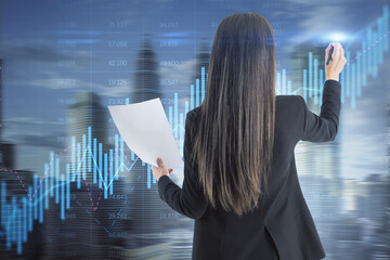 Poster - Back view of young businesswoman using glowing candlestick forex chart hologram on blurry city background. Trade, stock and global finance concept. Double exposure.