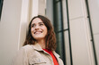 © contrastwerkstatt - Young woman leaning against a modern house facade and looking positively to the side