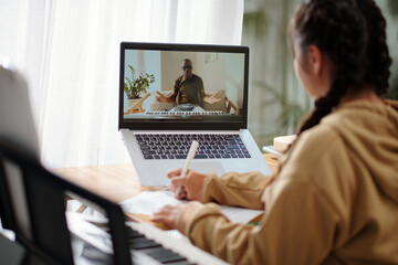 Teenage girl taking notes when having online class with music teacher