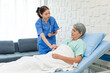 © Bangkok Click Studio - Asian professional successful female internship nurse in blue uniform with stethoscope visiting old senior elderly pensioner woman patient laying lying down on bed writing symptoms down on clipboard