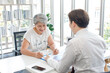 © Bangkok Click Studio - Asian old senior elderly female patient sitting in clinic office room listening to unrecognizable unknown doctor in white lab coat explaining showing tablet computer screen discussing about symptoms
