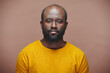 © pressmaster - Portrait of African American man with stubble in yellow shirt looking at camera against brown background