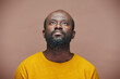 © pressmaster - Portrait of African American man looking up with pensive expression standing against brown background