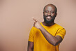 © pressmaster - Portrait of African American bearded man pointing at empty space and smiling at camera on brown background