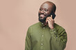 © pressmaster - Smiling African American man in green shirt having conversation on mobile phone isolated on brown background