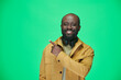 © pressmaster - Portrait of African American man in yellow jacket pointing at empty space and smiling at camera on green background