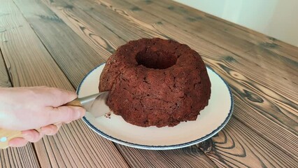 Canvas Print - Female hand cuts a piece of homemade chocolate vegan bundt cake with a knife and showing the inside of the cake