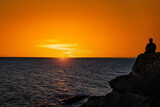 Fototapeta Niebo - Young couple watching the sunset on the Barbate beach next to the Trafalgar lighthouse, Cádiz