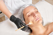 Beautician applies honey mask on woman face for moisturize face skin, anti aging cosmetic procedure in beauty spa salon. Cosmetologist in black gloves holds cosmetic brush for applying honey mask