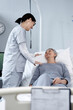 Vertical image of young female doctor examining elderly patient and talking to her during her visit in hospital ward