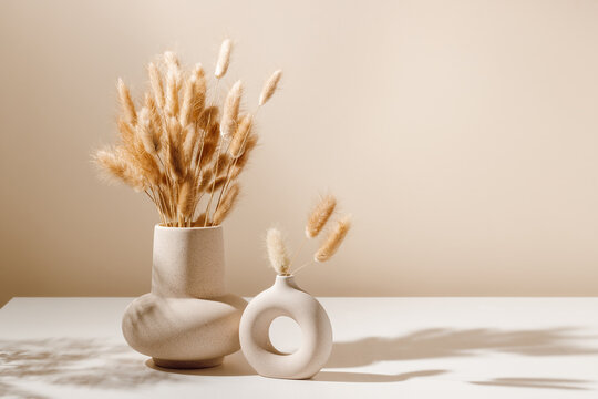 Stylish ceramic vase set on the table with dried lagurus grass bouquet with shadows, light brown wall background. Scandinavian vase on the table with copy space, minimal aesthetic interior decoration