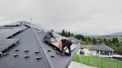 Wall Mural - Technicians building photovoltaic solar module station on roof of house. Men electricians in helmets installing solar panel system outdoors. Concept of alternative and renewable energy. Aerial view.