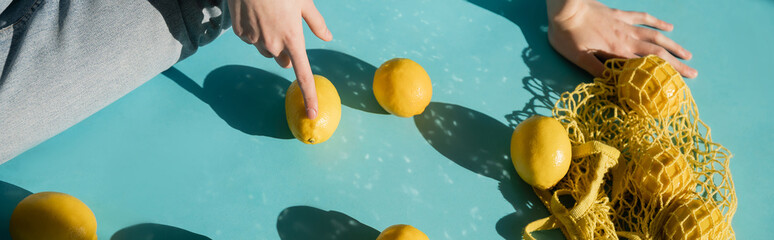 Wall Mural - cropped view of woman sitting near string bag and ripe lemons on blue, banner.