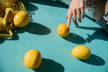 Canvas Print - cropped view of woman in shiny top with sequins posing near string bag and ripe lemons on blue.