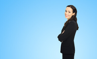 Sticker - Happy smiling attractive businesswoman, with copy space area for some slogan or advertising text. Confident brunette woman in black suit standing on sky blue background. Business ad concept.