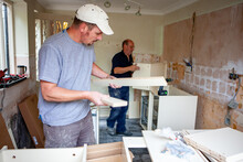 Kitchen Fitters: Flat Pack Build. A Pair Of Carpenters Building The Carcass To A New Fitted Kitchen. From A Series Of Related Images.