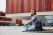 © Westend61 - Smiling woman with backpack sitting outside building