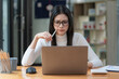 © Songsak C - Concerned female worker looking at laptop screen suspiciously, thinking about problem-solving, reading ambiguous emails or negative news. Concept of focus and concentration