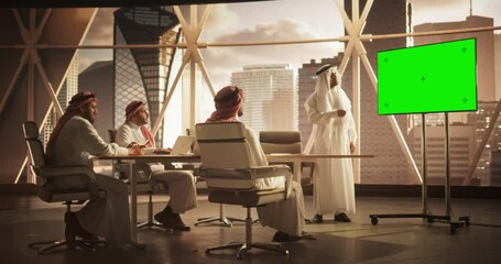 Wall Mural - Arab Businessman Shows Data to a Group of Saudi Investors. TV Screen with Green Screen Mock Up Display. Business Meeting Presentation in Conference Room in Modern Office