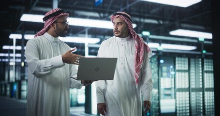 Poster - Middle Eastern Computer Engineer and Cybersecurity Specialist Work in Server Room, Talk, Perform System Maintenance Check with Laptop Computer. Specialists Doing Database Diagnostics in Data Center