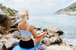 © makedonski2015 - An unrecognizable woman sits with her back to the camera while meditating on a rock by the sea.