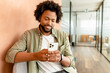 © Vadim Pastuh - Smiling african american business man with smartphone in hand looking screen and sitting indoor, male office employee, entrepreneur using smartphone, chatting and texting online