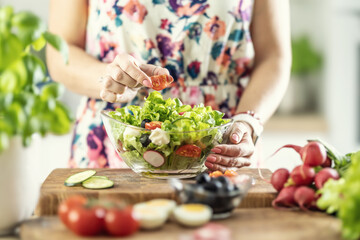 Wall Mural - A woman prepares a healthy salad and puts a sliced tomato in a bowl