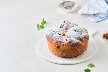 Wall Mural - Twisted yeast cake with raisins sprinkled with powdered sugar on a white ceramic board against a light concrete background. Easter concept.