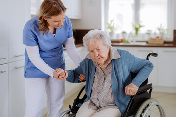 Nurse helping senior woman to stand up from wheelchair.