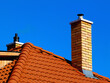 modern brick finished chimneys stack with white concrete cap stone, bright brown red clay roof tiles and metal flashing under blue sky on crisp blue winter day in bright sunlight. construction concept