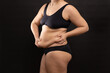 © Юля Бурмистрова - Overweight woman in black underwear massaging belly fat folds by hands, side view. Flaunt figure imperfections, cellulite body. Studio portrait isolated on black. Body positive, plus size people.
