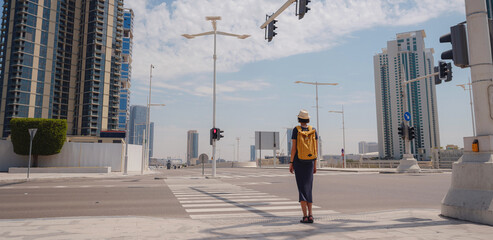 travel to the United Arab Emirates, Happy young asian female traveler with backpack and hat stands at crossroads waiting for green light of traffic light.