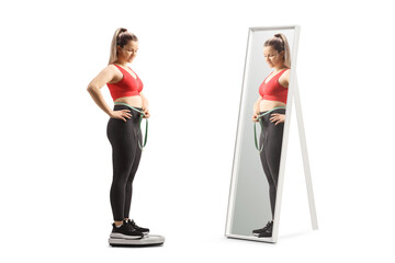 Sticker - Young woman in sportswear on a weight scale measuring waist and standing in front of a mirror