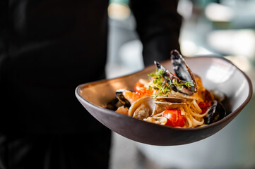 chef hand hold Italian spaghetti pasta marinara with Clams, Prawns, Mussels, tomato, Seafood Cocktail in plate