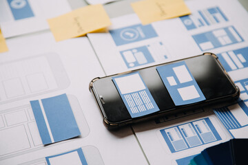 Close up ux developer and ui designer brainstorming about mobile app interface wireframe design on table with customer breif and color code at modern office.Creative digital development agency