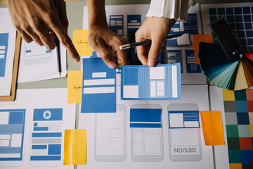 Close up ux developer and ui designer brainstorming about mobile app interface wireframe design on table with customer breif and color code at modern office.Creative digital development agency