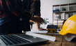 © ARMMY PICCA - Three colleagues discussing data working and tablet, laptop with on on architectural project at construction site at desk in office