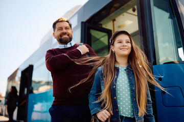 Happy girl and her father getting off a bus at station.