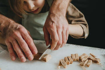 Wall Mural - Unrecognizable father and daughter in aprons cut the dough on a white background against a dark wall