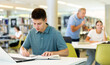 © JackF - Concentrated young man checking plans in calendar while studying in the library and using laptop