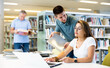 © JackF - Friendly young woman offering assistance to male friend studying, finding information at university library