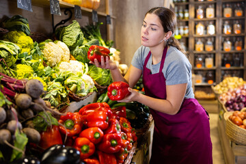 Wall Mural - Young woman seller holding bell peppers in greengrocer shop