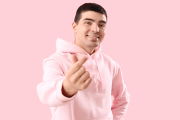 Wall Mural - Young man making heart with his fingers on pink background